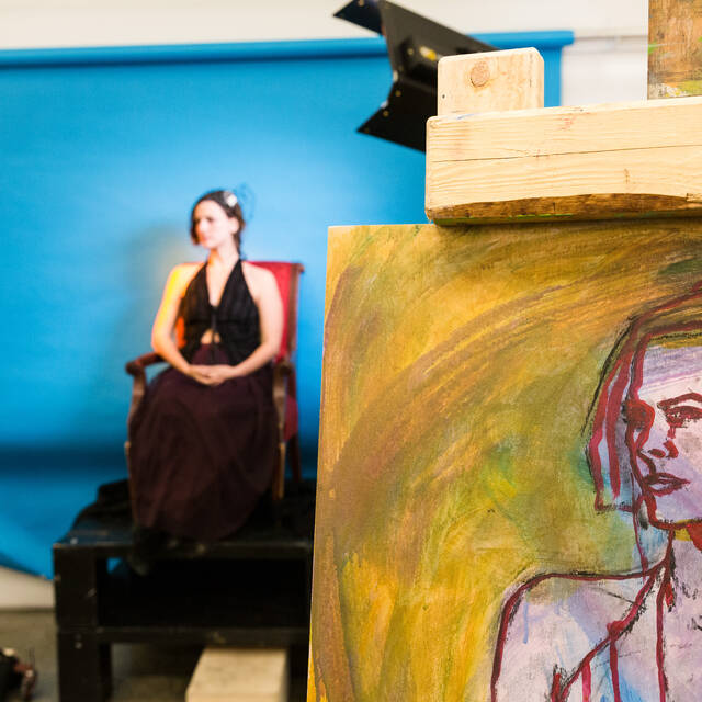 An art model sits for a painting class. An student painting of the models is featured in the foreground