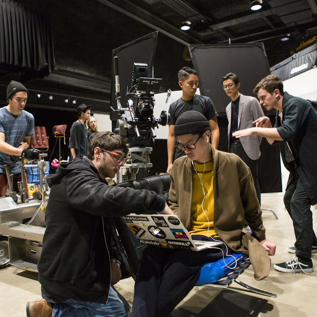 ArtCenter film students review captured footage on a laptop while other students prepare for the next shot in the background. 