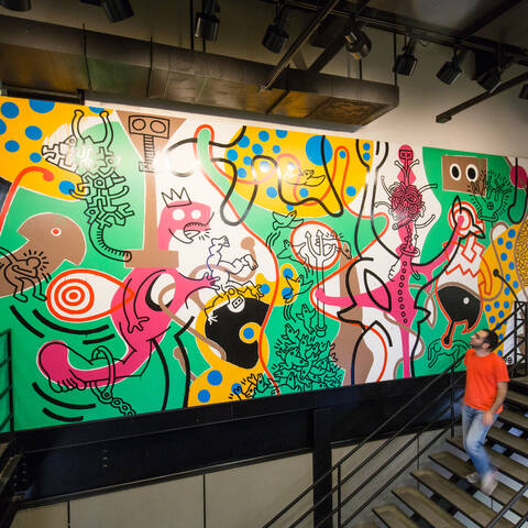 Student walking down stairs in front of Keith Haring mural