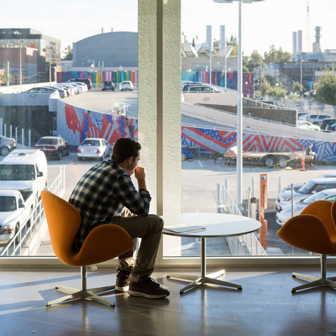 A students sits in an orange chair looking out the second floor window toward the parking lot
