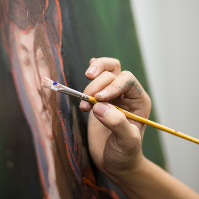 Hand holding paintbrush painting a face on a canvas