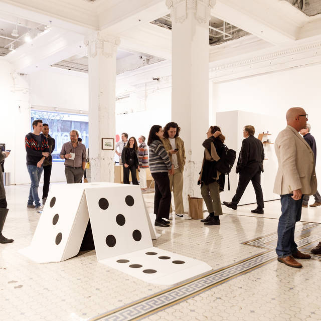 Giant die on a marble floor surrounded by people at a gallery opening