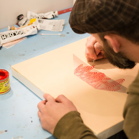 A grad art student paints on wood with red paint 