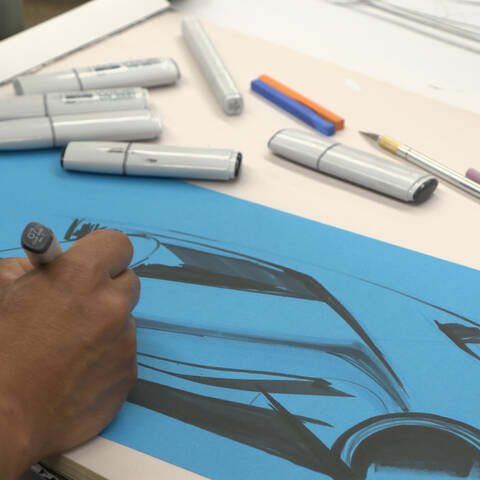 hand sketching car on blue paper with markers on table