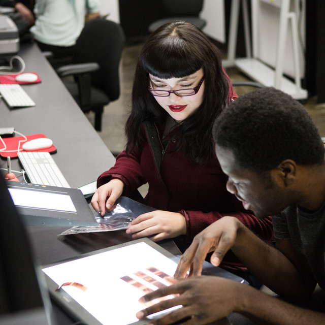 Two students review film negatives on a lightbox