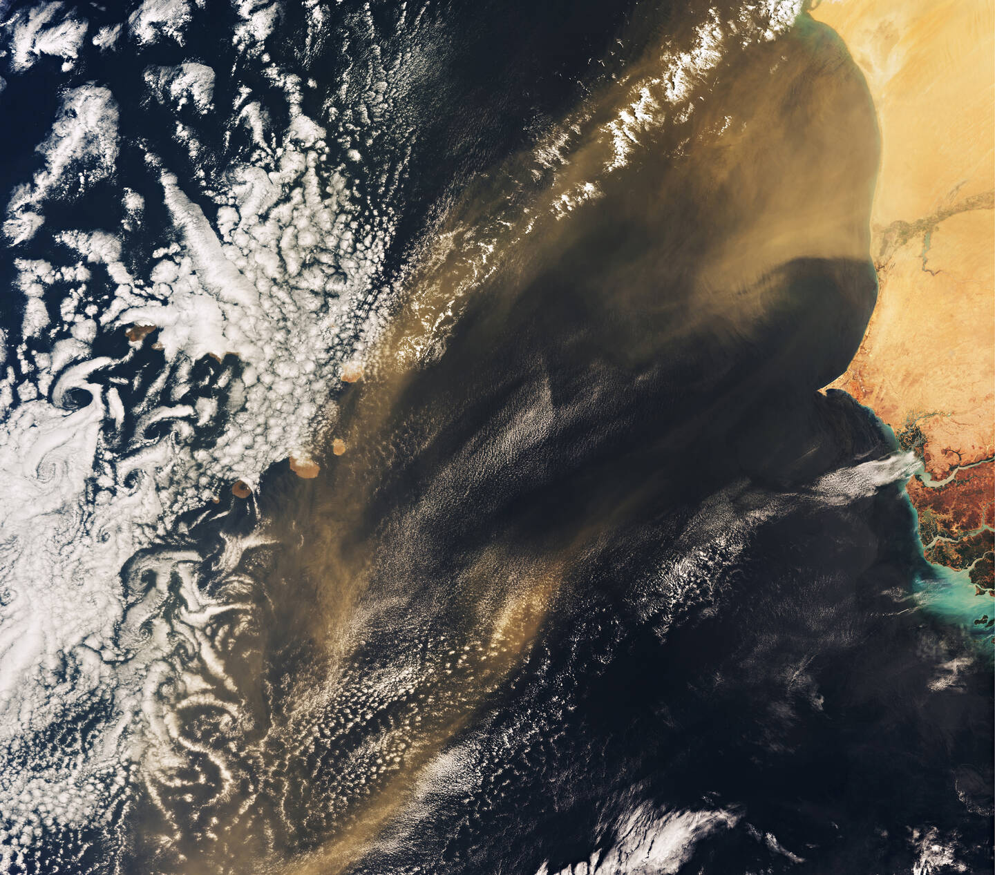 Several+of+the+small+islands+that+make+up+the+Republic+of+Cape+Verde+can+be+seen+beneath+the+clouds.+These+volcanic+islands+lie+in+the+Atlantic+Ocean+about+570+kilometers+%28355+miles%29+off+the+west+coast+of+Africa%2C+which+is+on+the+right.+The+most+striking+thing+in+this+image%2C+however%2C+is+the+dust+and+sand+being+carried+by+the+wind+toward+Cape+Verde+from+the+Sahara+and+an+adjacent+region.+This+sand+also+fertilizes+the+ocean+with+nutrients+and+promotes+the+growth+of+phytoplankton%2C+which+are+microscopic+plants+that+sustain+the+marine+food+web.+The+iron+in+the+dust+is+particularly+important.+Without+iron+mammals+cannot+make+hemoglobin+to+transport+oxygen+through+the+bloodstream%2C+and+plants+cannot+make+chlorophyll+to+photosynthesize.+Around+80+percent+of+iron+in+samples+of+water+taken+across+the+North+Atlantic+originates+from+the+Sahara.+May+30%2C+2018.