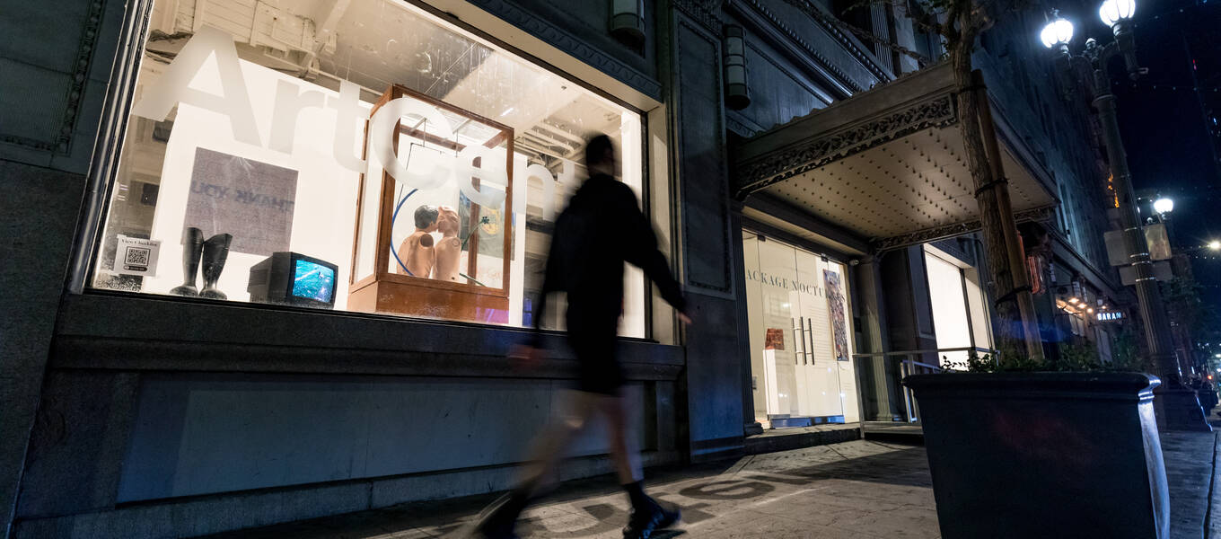 A person walks past Package Nocturnes, installed in the windows of ArtCenter DTLA, at night. Photo by Juan Posada.