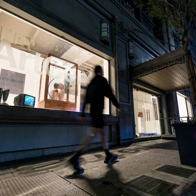 A person walks past Package Nocturnes, installed in the windows of ArtCenter DTLA, at night. Photo by Juan Posada.