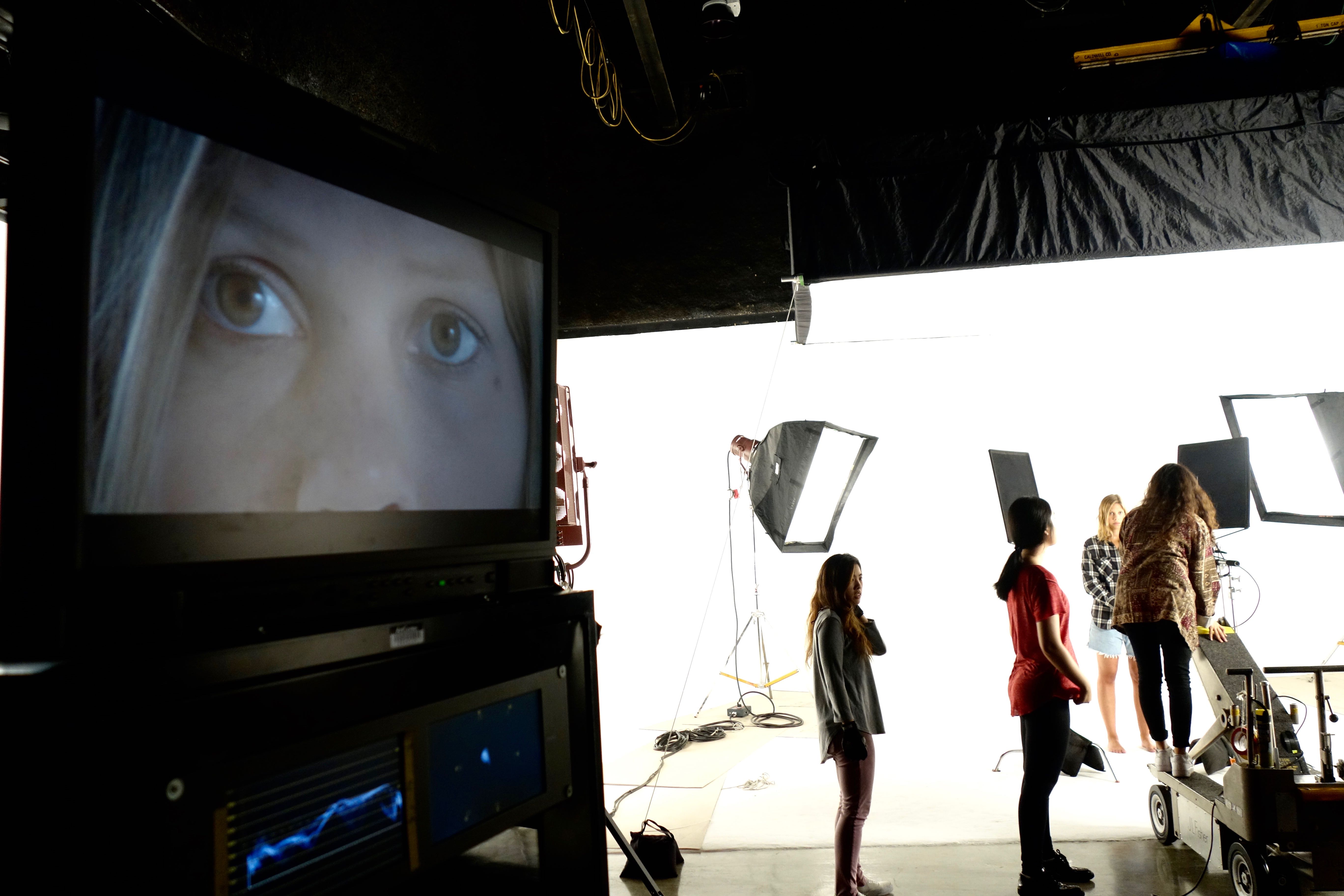 ArtCenter film students on set shooting a project with a large screen close up of a young woman