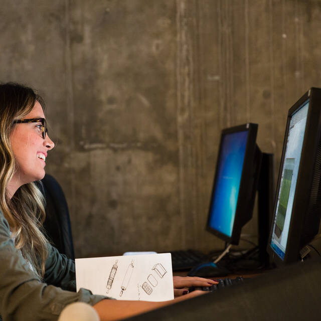 Blonde woman with glasses smiles at a computer screen 