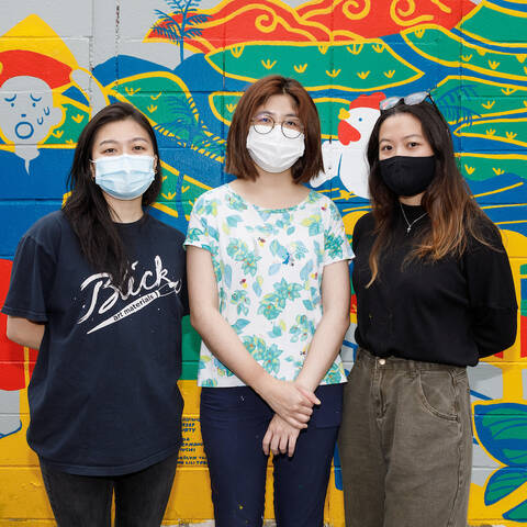 Three students stand in front of a colorful mural. 