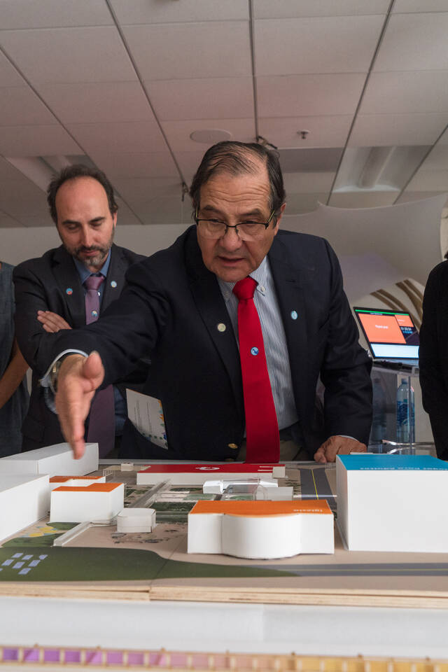 Founder and Executive President Dr. Jorge Rojas Zegers (center) of COANIQUEM reviews a 3D environmental student project laid out on a table, as students, faculty and others listen.