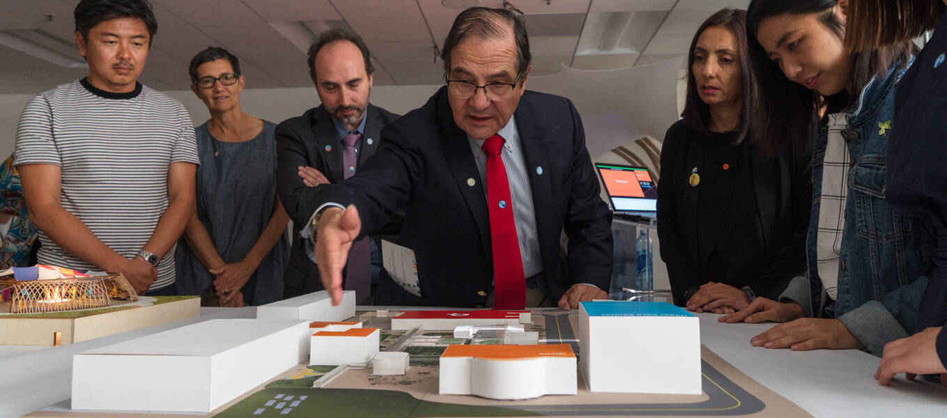 Founder and Executive President Dr. Jorge Rojas Zegers (center) of COANIQUEM reviews a 3D environmental student project laid out on a table, as students, faculty and others listen.