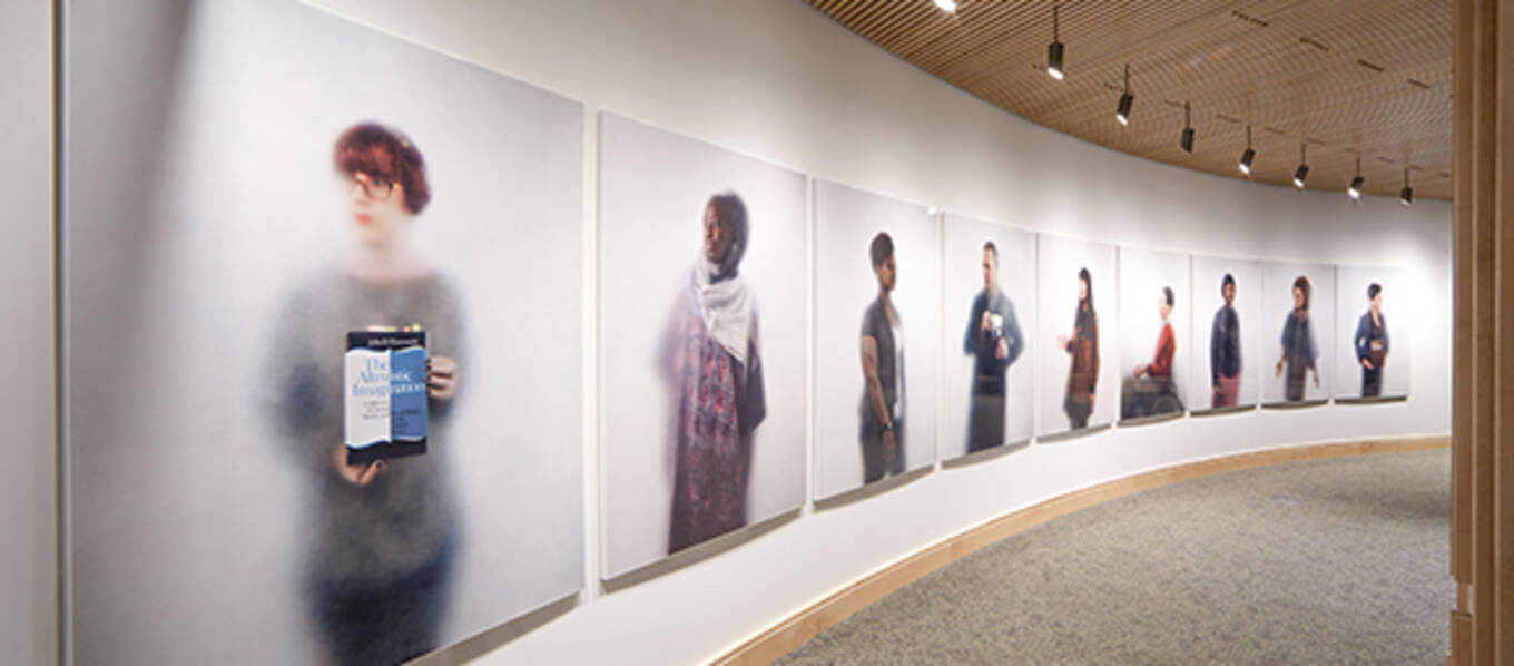 Large portraits hang on a wall in a curved hallway with a wood slat celing
