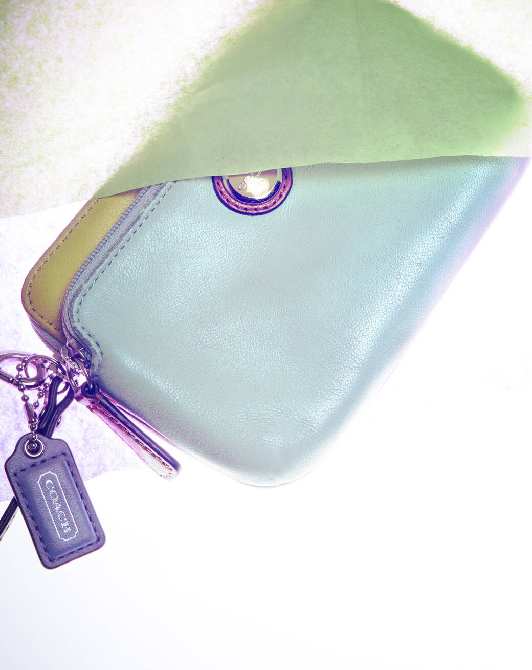 A green and yellow leahter Coach Double Zip Wallet, with purple accents, lying between two translucent sheets of paper.