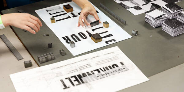 hands of students working on letterpress with a sheet of paper that reads live your life
