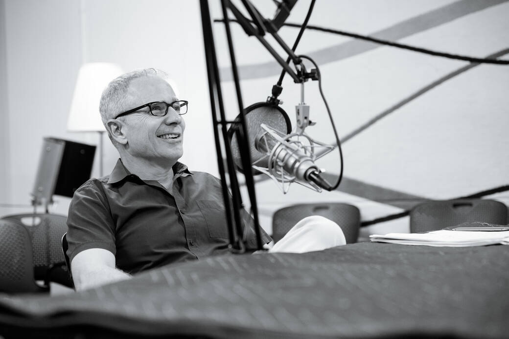 Black-and-white photograph of ArtCenter President Lorne M. Buchmanl, dressed casually, laughing, and leaning back in front of a large microphone, during a recording session of his Change Lab podcast.