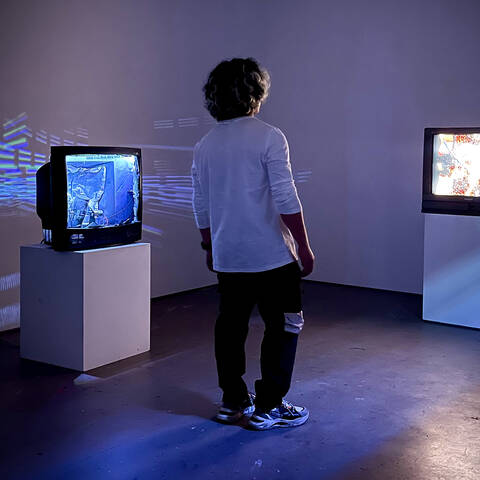 A man walks between two vintage tv sets displaying media art in a gallery setting.