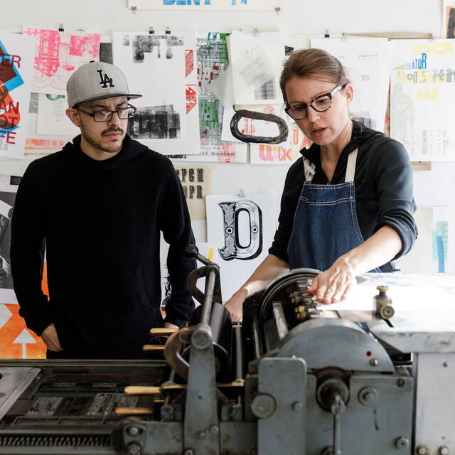 Student and teacher discuss project around a letterpress machine. 