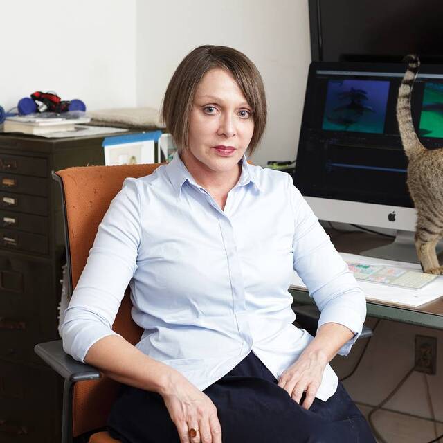 /Diana Thater sitting at her desk with a cat standing on desk