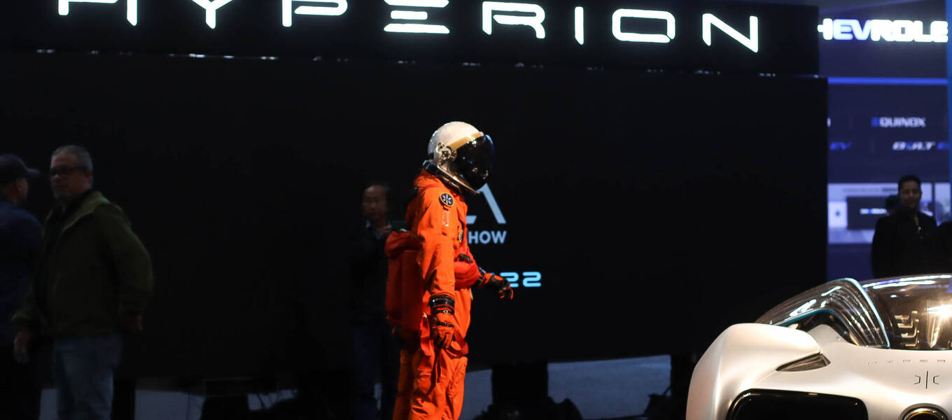 a statue of a person in an orange spacesuit standing next to Hyperion car