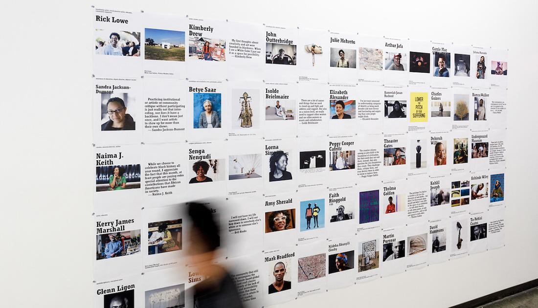 blurry person walking by posters on a wall. The posters feature Black artists