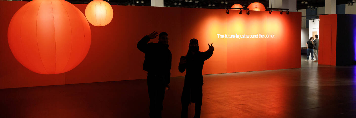 Grads take photos in front of an orange wall that reads 