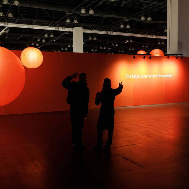 Grads take photos in front of an orange wall that reads 