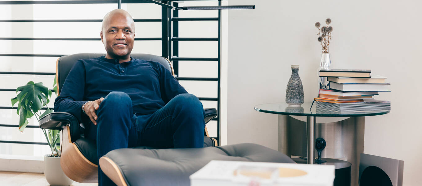 Kevin Bethune seated in his Redondo Beach studio, with books in front of him (out of focus) on a coffee table and to his left, on an accent table.