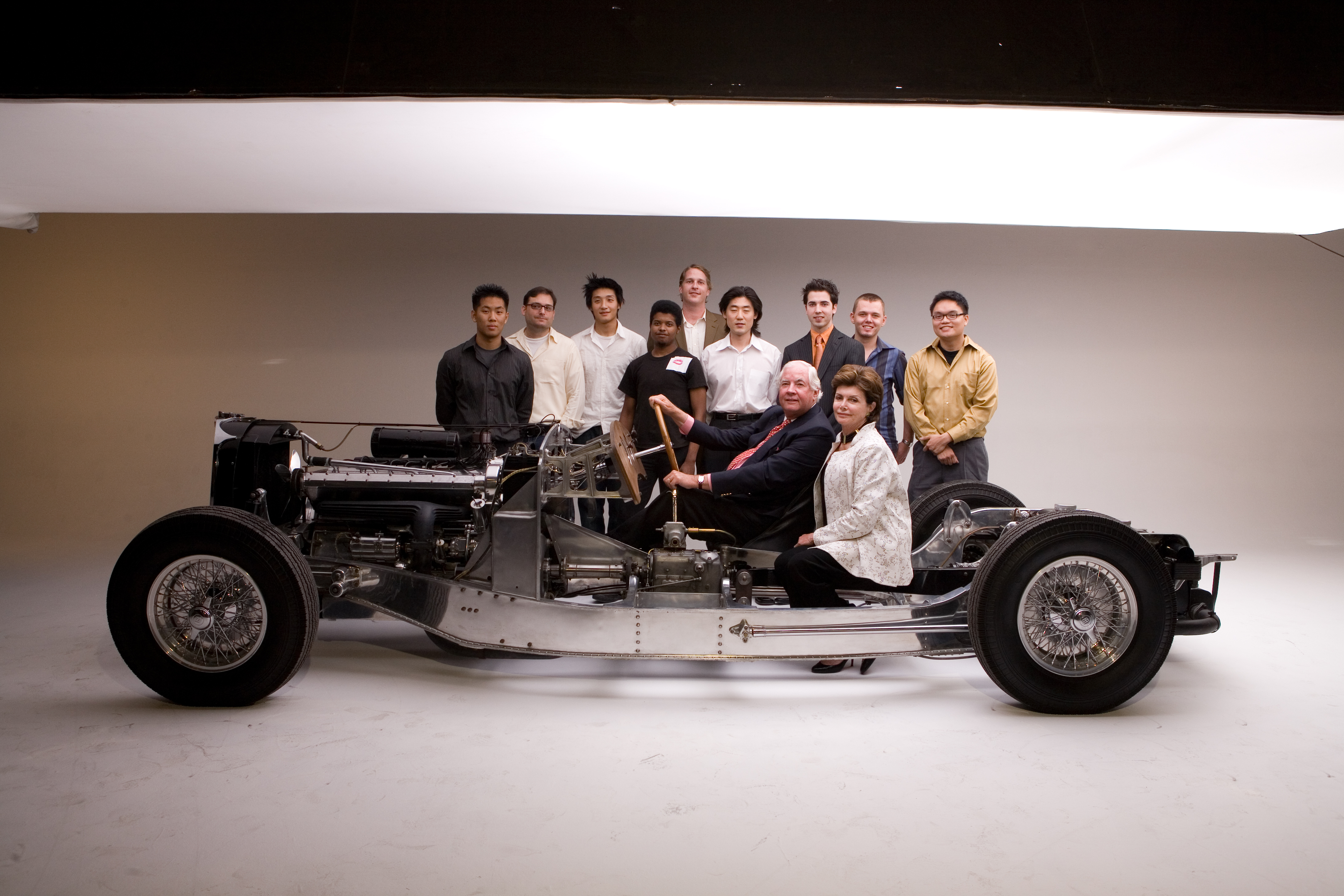 A photo of Peter and Merle Mullin sitting in a Bugatti and a group of students at ArtCenter College of Design.