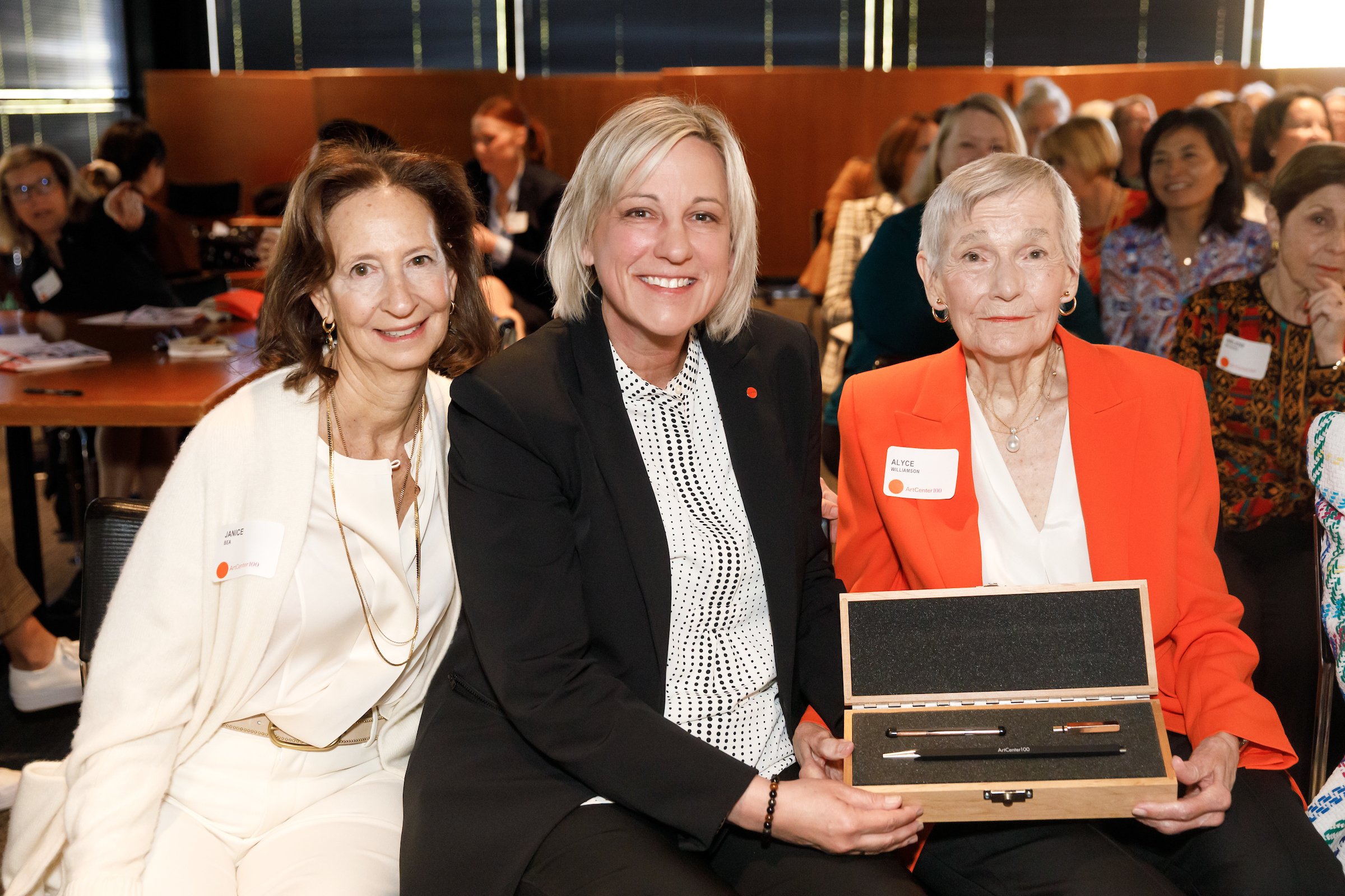 Current ArtCenter100 President Janice Bea with ArtCenter President and CEO Karen Hofmann presenting the honorary engraved pencil to ArtCenter100 founder Alyce de Roulet Williamson on November 3, 2023 in Pasadena. © ArtCenter College of Design/Juan Posada 