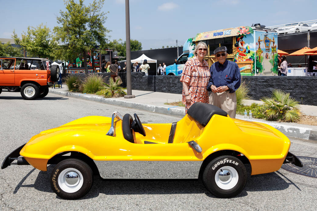 President Karen Hofmann and alum Bob Gurr (BS 52), both wearing sunglasses, stand behind a bright yellow-colored 1967 Autopia Mark VII which Gurr designed