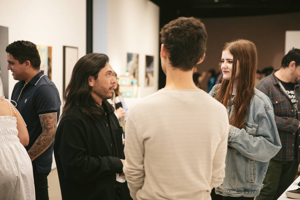 Alum, faculty and IdentificarX curator Ryan Perez (BFA 08), left, speaks with two guests at the exhibition