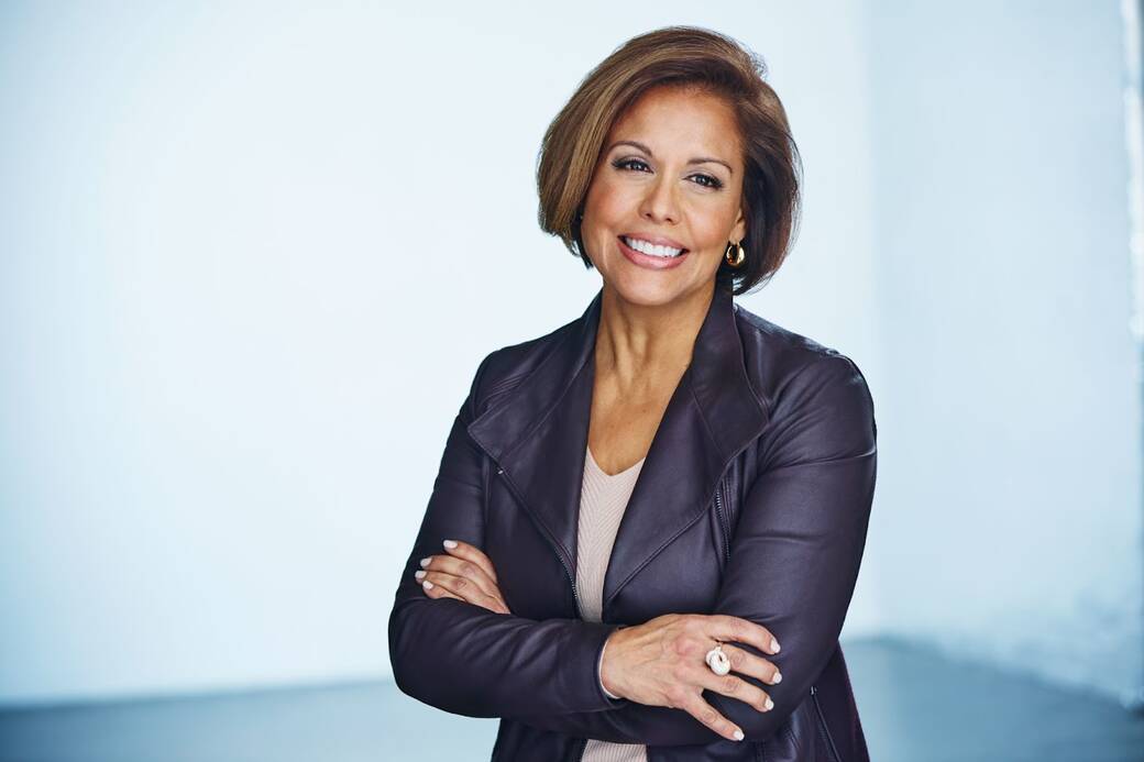 A portrait of Michele Ruiz, smiling, with a white wall behind her