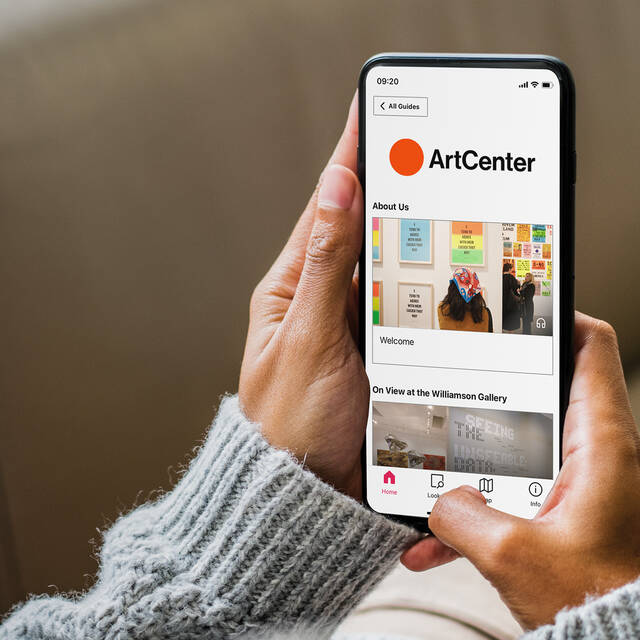 Hands holding a smartphone displaying the ArtCenter Bloomberg Connects app, showcasing exhibition content.