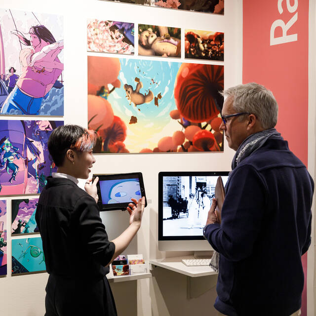 Graduating student presenting their portfolio to a recruiter at the grad show, standing beside a display of their creative work.