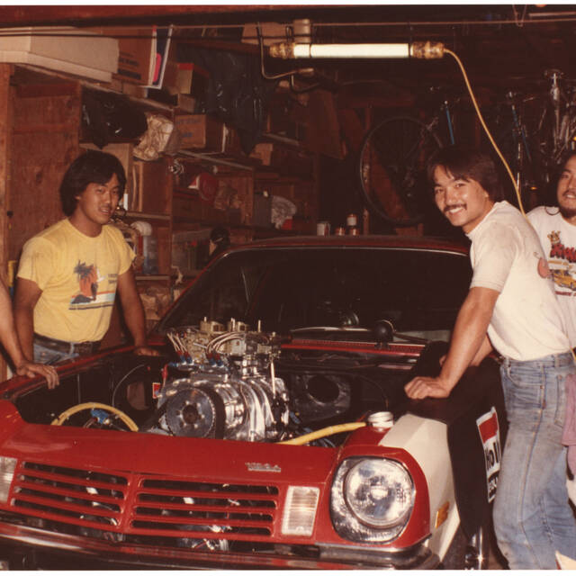 Four men gathered around a red, hoodless car with its engine exposed during Nisei Week Cruise, 1982. Photo by Tod Kaneko.