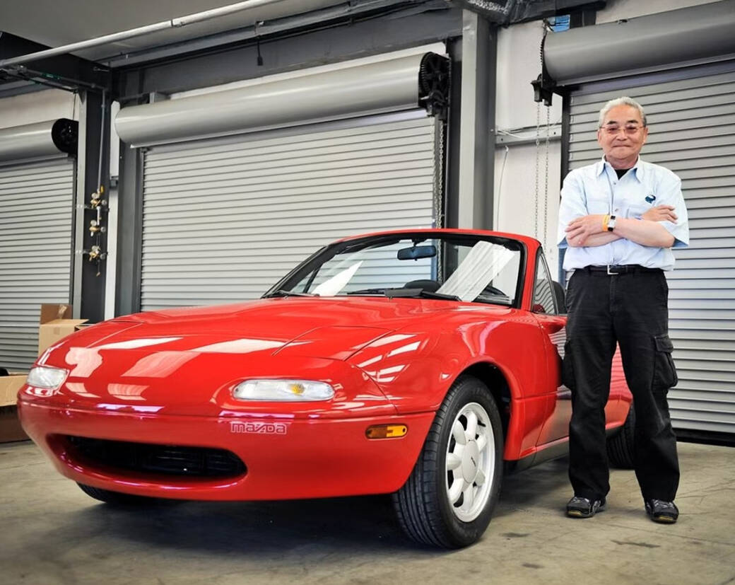 Tom Matano stands inside a well-lit garage next to a red Mazda MX-5 Miata.