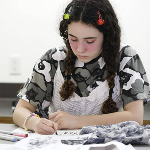 /High school student sketching a fashion figure in Fashion Illustration class at ArtCenter Summer Extension, rendering garments and fabric details from a live model.