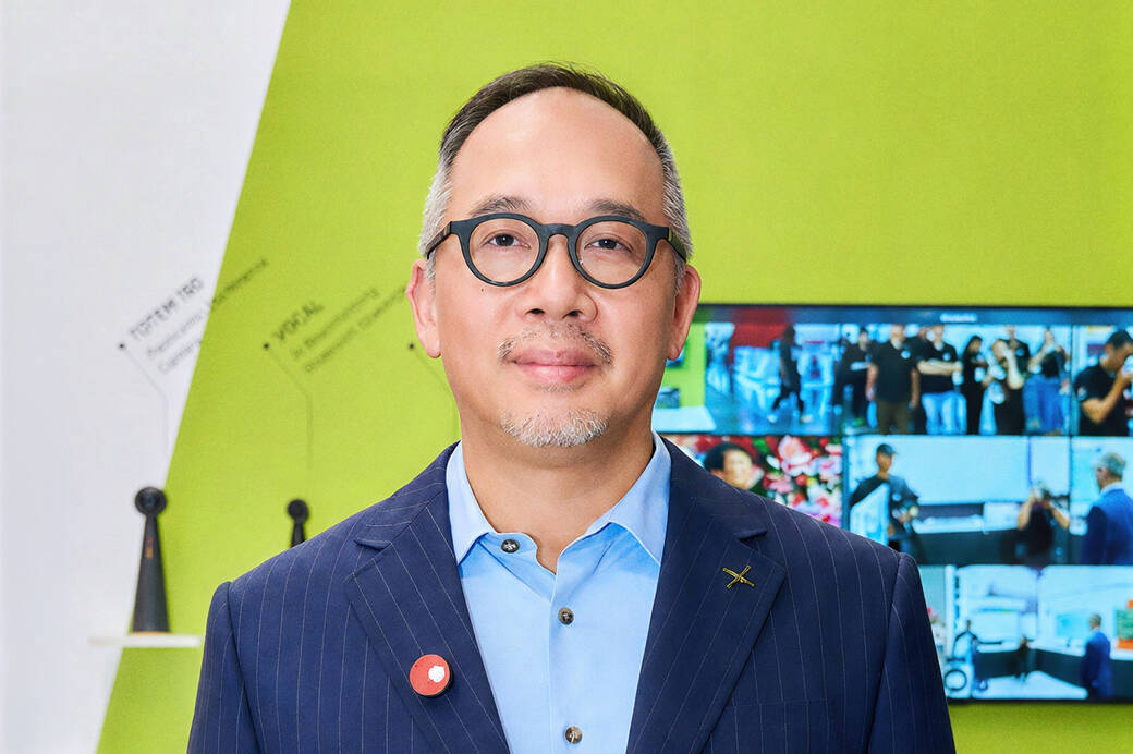 Royce Hong, wearing a blue blazer, at a business event, in front of a lime green wall
