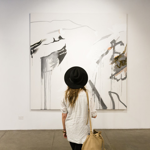 A woman in a black had looks at an abstract painting in the student gallery