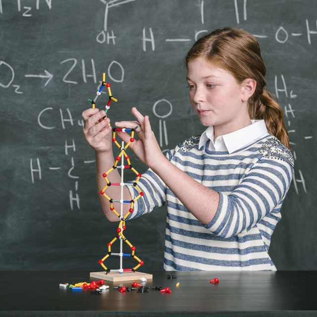 /image of a school aged girl building a DNA model in front of a chalk board