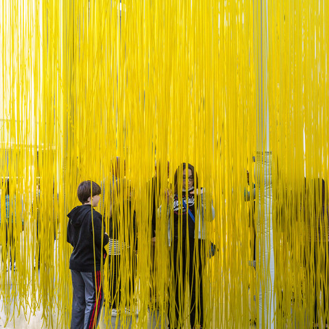 people walking through yellow strands at an art exhibition