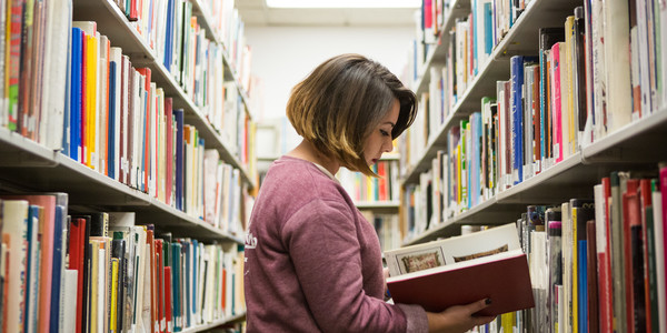 An ArtCenter student looks at a book while browsing the library stacks