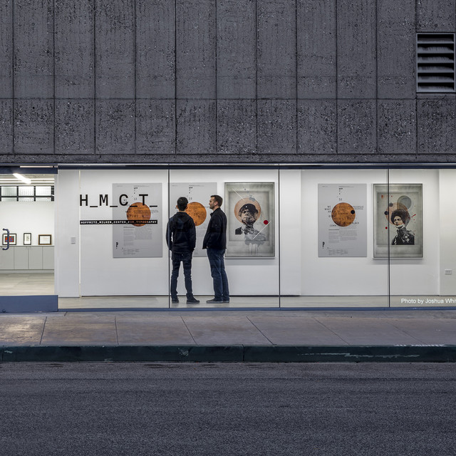 Two men talk in front of the large street facing gallery windows at HMTC Gallery