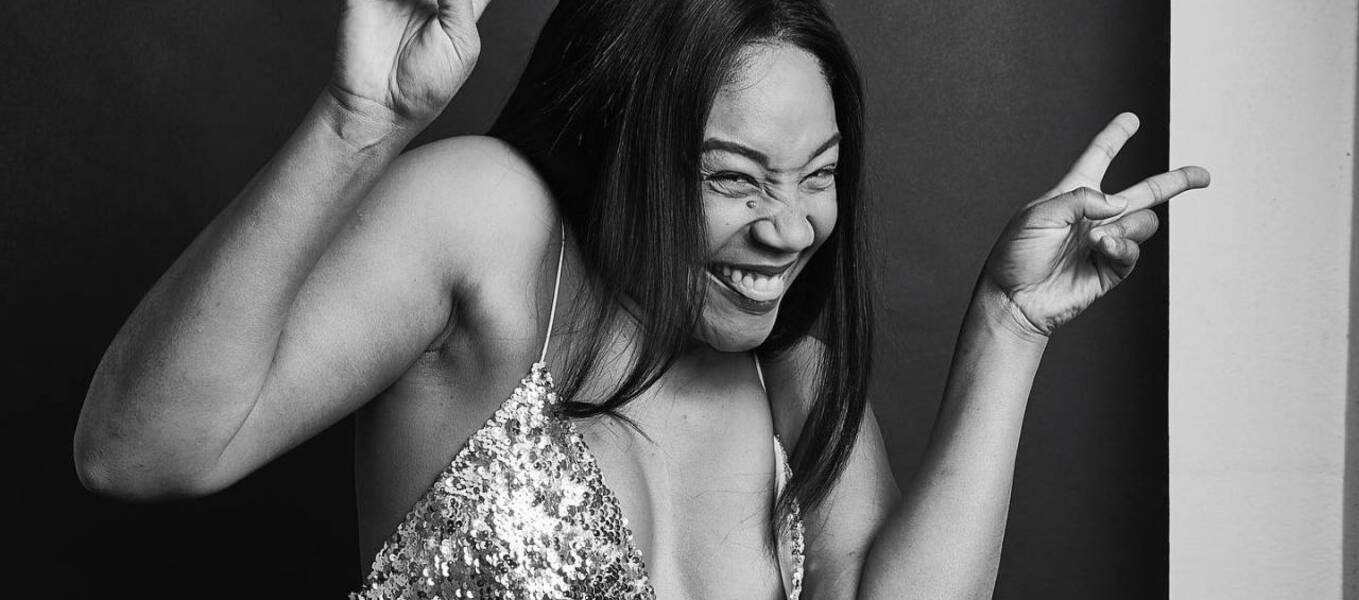 Black and white photo of woman in sparkly dress smiling and giving peace signs with both hands