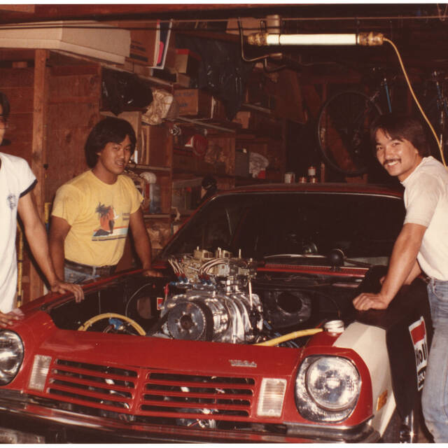 Four men gathered around a red, hoodless car with its engine exposed during Nisei Week Cruise, 1982. Photo by Tod Kaneko.